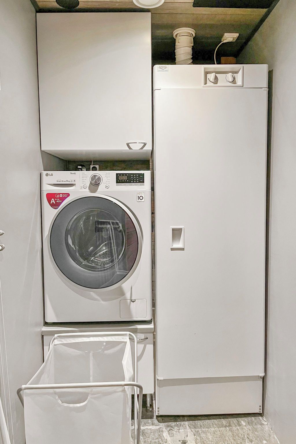 A compact laundry room with a front-loading washer and dryer, a small storage bin, and a tiled floor.