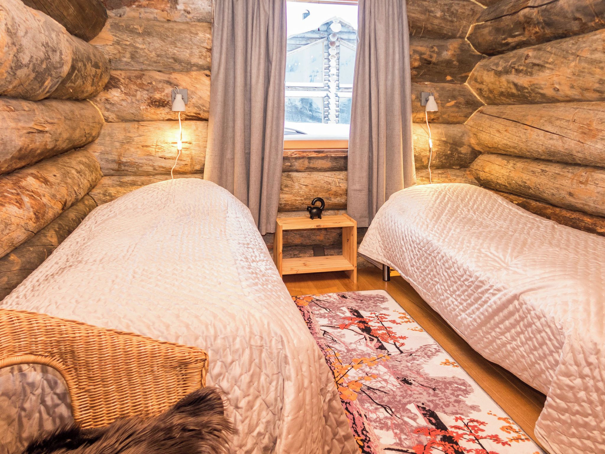 Une chambre confortable dans un chalet en rondins, avec deux lits, une petite table et une fenêtre avec des rideaux.