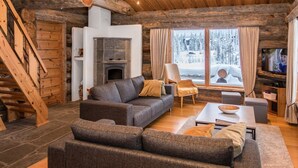 Ein gemütliches Blockhaus-Interieur mit Kamin, einer Couch, einem Sessel und einem Fernseher.