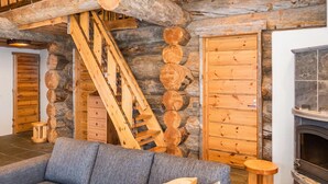 Ein Blockhaus-Interieur mit einer Holztreppe, einem Kamin und einem grauen Sofa.