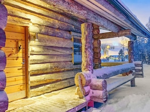 A log cabin with a wooden door, a bench, and a snow-covered ground.