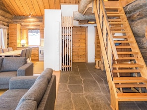 A log cabin interior with a stone floor, wooden furniture, and a wooden staircase.