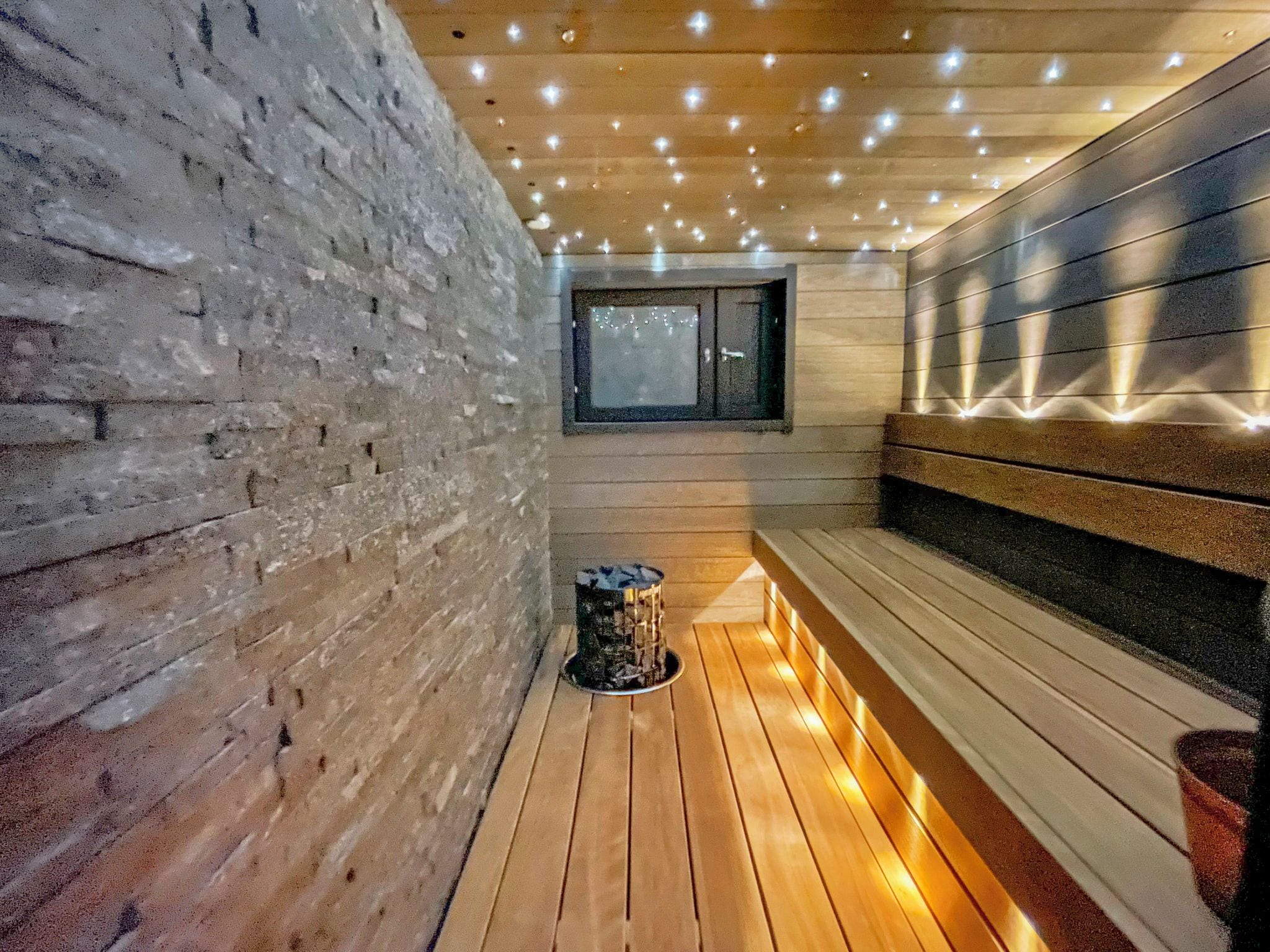 Un intérieur en bois avec un banc, une petite poubelle et une fenêtre.