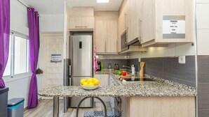 A compact kitchen with a granite countertop, stainless steel appliances, and a small dining area with a chair. - Apartment Cloud by Interhome (Segur de Calafell)