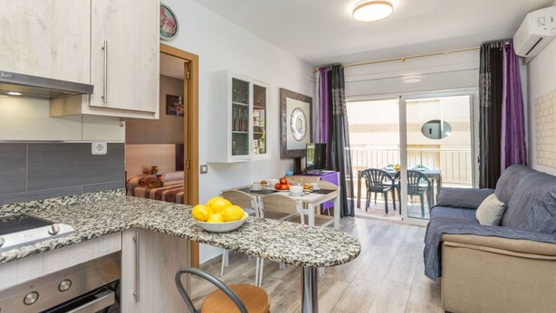 A modern kitchen with granite countertops, a dining area with a table and chairs, and a living area with a sofa. - Apartment Cloud by Interhome (Segur de Calafell)