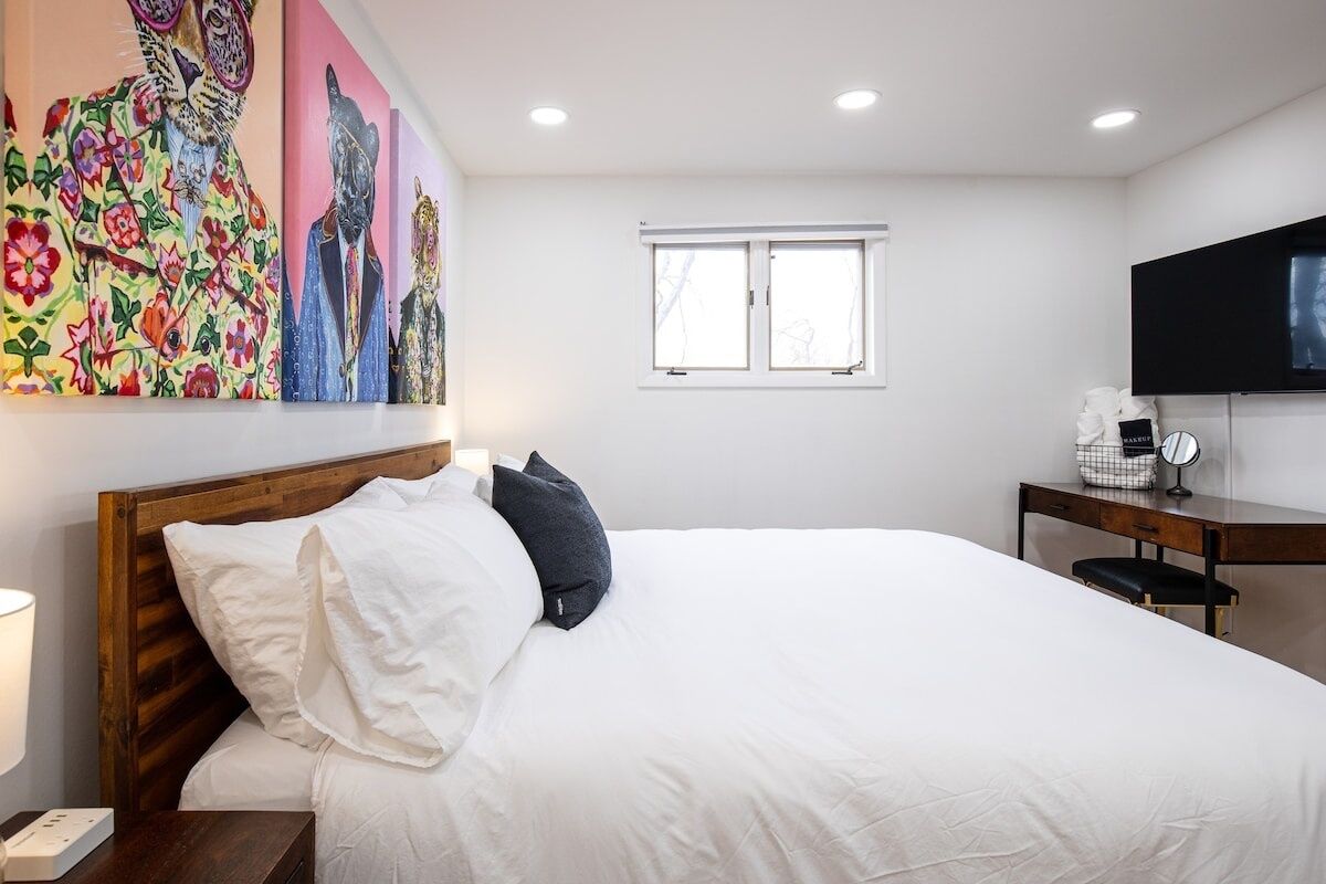 A hotel room with a large bed, a wooden headboard, a desk with a chair, a flat-screen TV, and a window.