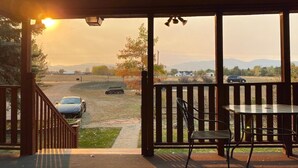 A covered outdoor area with a table and chairs, a view of a road with cars, and a sunset in the background.