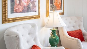 A room with two white armchairs, a green lamp, and two framed paintings on the wall.