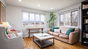A living room with a beige sofa, a white armchair, a wooden coffee table, and a bookshelf.