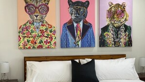 A bedroom with a bed, pillows, and three paintings on the wall.