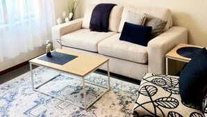 Een woonkamer met een beige bank, een houten salontafel en vloerkleden met een patroon.