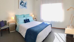 Een slaapkamer met een bed, twee nachtkastjes, een stoel, een hanglamp en een raam met dunne gordijnen.