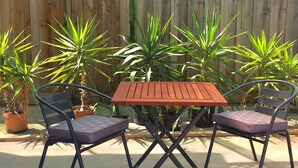 Een terras buiten met een houten tafel en twee stoelen, omringd door potplanten.