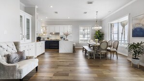 A spacious kitchen with white cabinets, a marble island, and a dining area with a bench and chairs. - Kemah's Bayfront Getaway with Pool (Kemah)