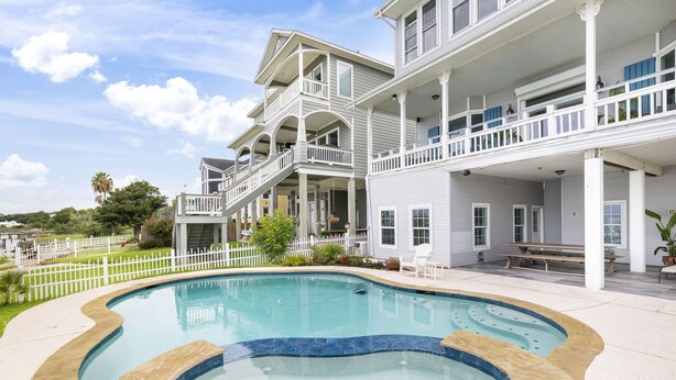 A two-story building with a swimming pool, a white fence, and a bench. - Kemah's Bayfront Getaway with Pool (Kemah)