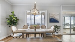 A dining room with a large wooden table, six chairs, a chandelier, and potted plants. - Kemah's Bayfront Getaway with Pool (Kemah)