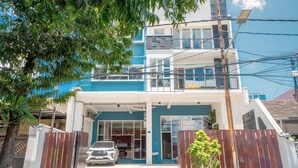Un edificio de dos pisos con fachada azul y blanca, una entrada con portón y un coche estacionado adelante.