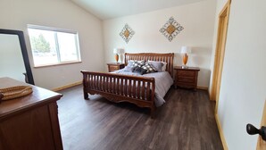 A bedroom with a wooden bed, two bedside tables, a ceiling fan, and decorative wall art. - Beaverhead House Rental (Dillon)