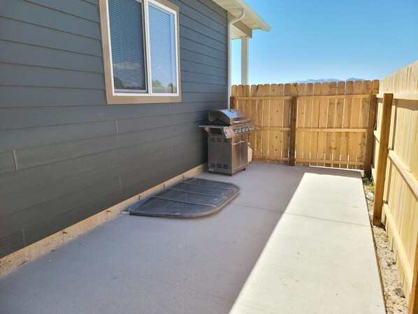 A patio with a barbecue grill, a wooden fence, and a house with siding.