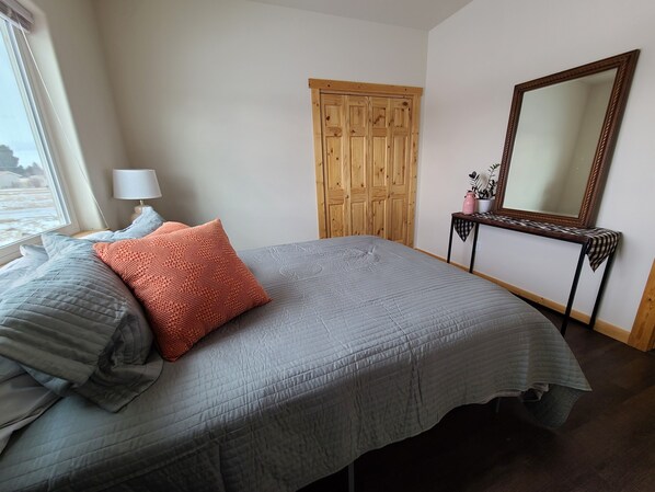 A bedroom with a bed, a wooden wardrobe, a bedside table with a lamp, and a large mirror.
