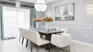 Ein Esszimmer mit einem großen Tisch, gedeckt für sechs Personen, weißen Stühlen, einer Chandelierleuchtre und einem Gemälde an der Wand.
