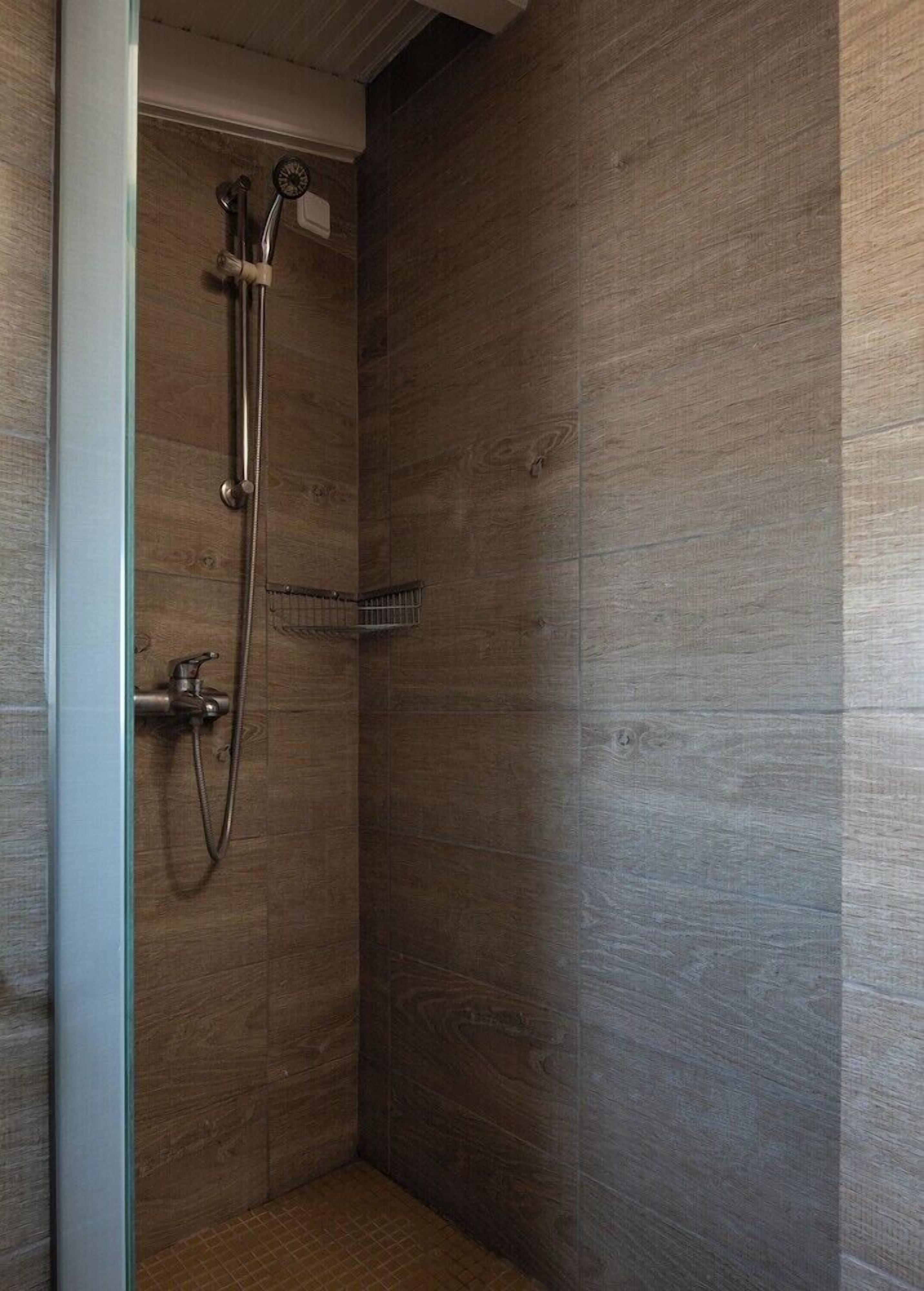 A walk-in shower with a wooden wall and a metal showerhead.