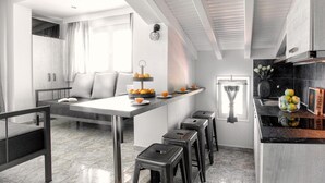 A modern kitchen with a central island, bar stools, and a dining area with a sofa and pillows. - Poseidon Apartments (Skiathos)