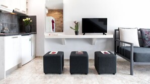 A modern living room with a flat-screen TV, a sofa, and three ottomans. - Poseidon Apartments (Skiathos)