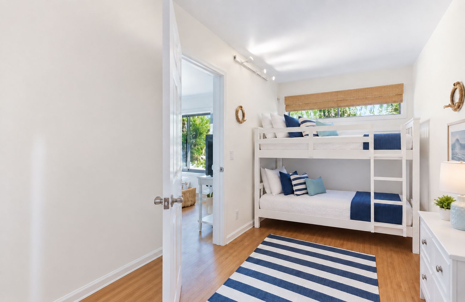 A bedroom with bunk beds, a wooden floor, a striped rug, and a window with a view of greenery.
