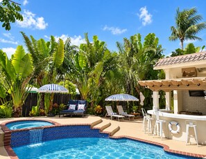 A swimming pool with a tiled edge, surrounded by lounge chairs and umbrellas, with palm trees in the background. - Just steps to the beach, sleeps 16, Golf cart, Dolphin Beach House huge pool! (Fort Lauderdale)