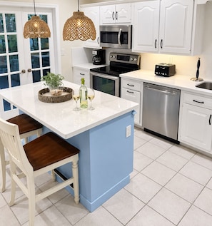 A kitchen with white cabinets, a blue island, stainless steel appliances, and wicker pendant lights.