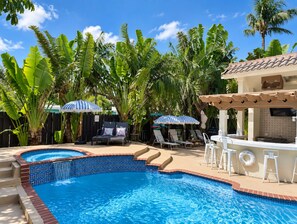 A swimming pool with lounge chairs and umbrellas, surrounded by tropical plants.