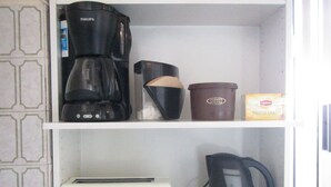 Uno scaffale in cucina con una macchina da caffè, un tostapane, un bollitore e una tazza da caffè.