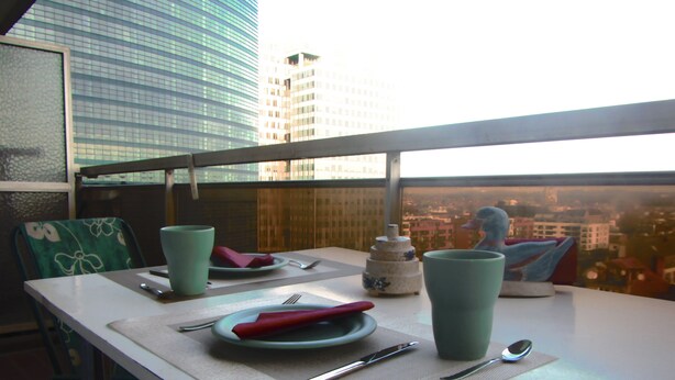 Tavola imbandita con piatti, posate e un oggetto decorativo, con vista sui palazzi attraverso una finestra.