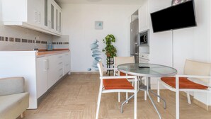 Une cuisine moderne avec des meubles blancs, une table à manger avec des chaises, un téléviseur à écran plat et une plante en pot.
