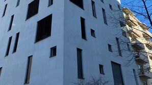 Un bâtiment moderne de couleur blanche, doté de nombreuses fenêtres et de balcons, avec un toit plat et une combinaison de fenêtres de forme rectangulaire et carrée.