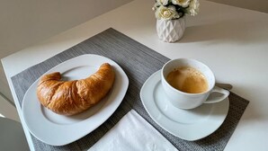 Un croissant sur une assiette blanche, une tasse de café sur une soucoupe et un vase de fleurs blanches sur une table.
