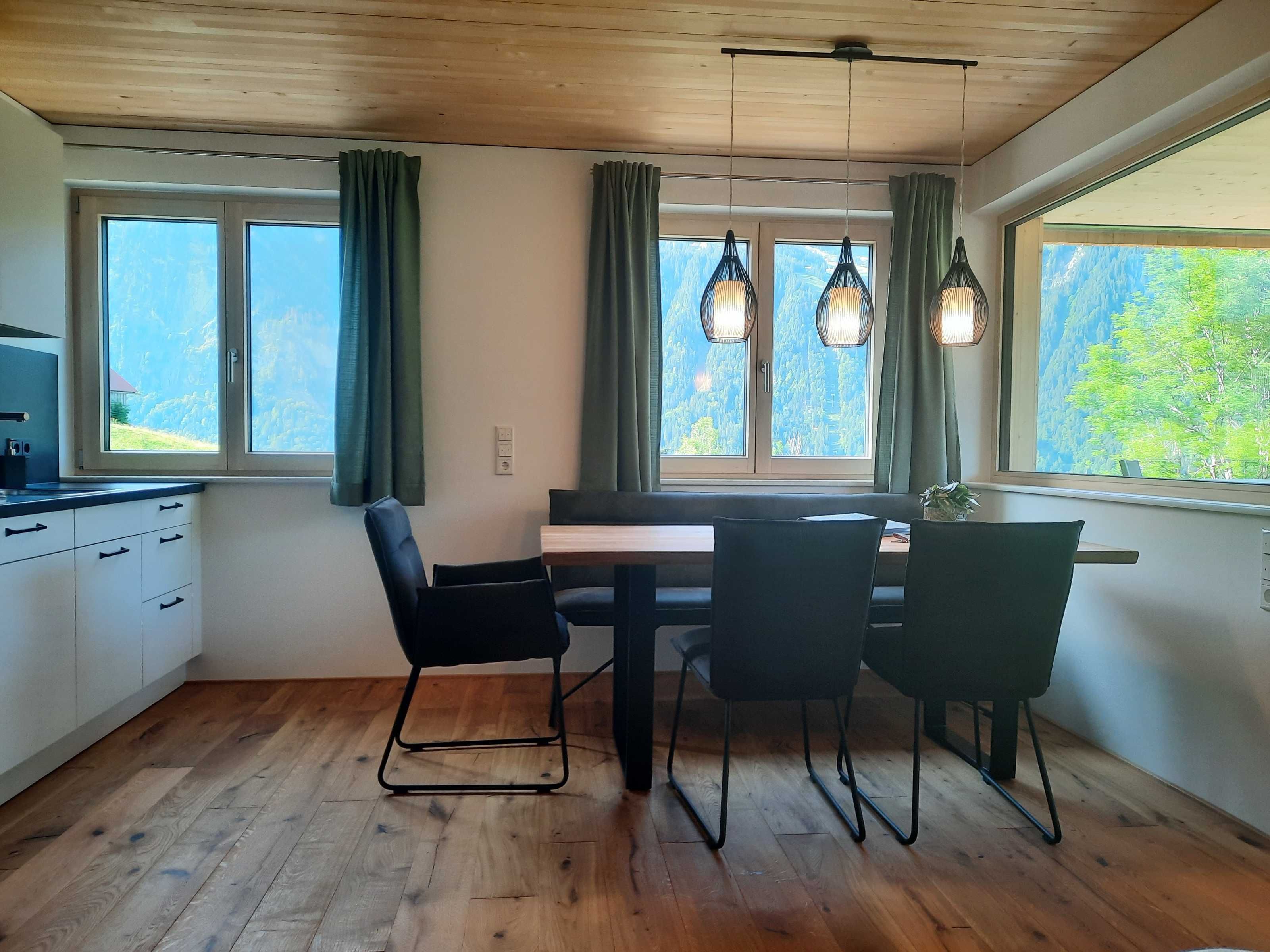 Eine moderne Küche mit Holzboden, einem Essbereich mit Tisch und Stühlen sowie großen Fenstern mit Vorhängen.