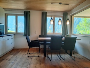 A modern kitchen with wooden flooring, a dining area with a table and chairs, and large windows with curtains. - Sunnseitn Vacation Apartment - Panoramahof Bergglück (Mellau)