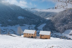 Un paisaje montañoso cubierto de nieve con dos edificios de madera, uno con garaje.