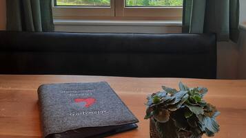 Ein Zimmer mit einem großen Fenster, einem Tisch mit einem Buch und einem Schlüsselanhänger, sowie einer Topfpflanze.