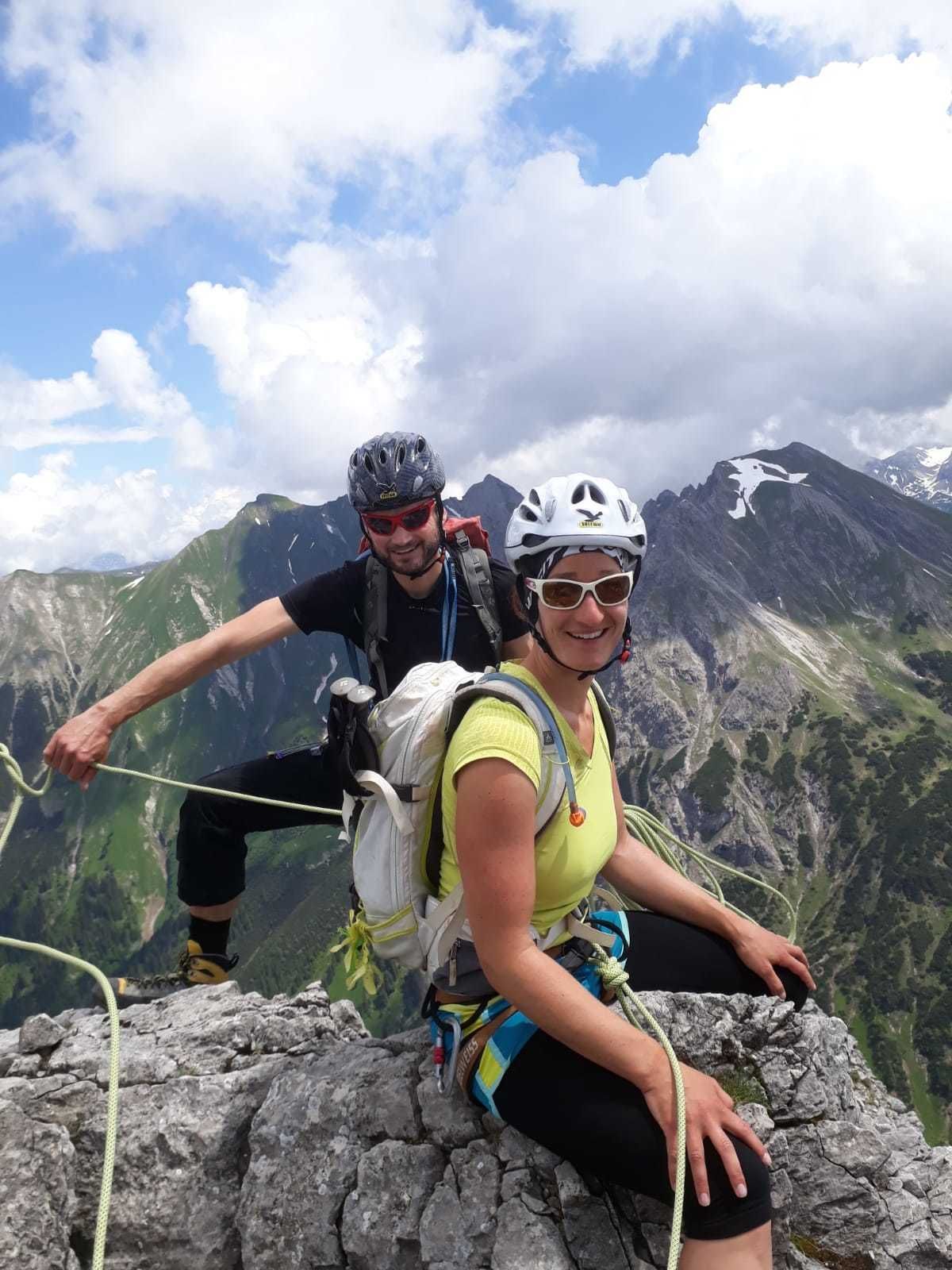 Två personer på en bergstopp med ett stenigt landskap och en bergskedja i bakgrunden.