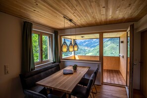 Un interior de madera con una mesa de comedor, sillas, un banco y grandes ventanales que ofrecen vistas a la montaña.