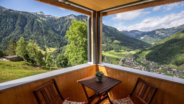 A balcony with wooden furniture, a small table, and a view of a mountainous landscape. - Vacation apartment Sunnseitn - Panoramahof Bergglück (Mellau)