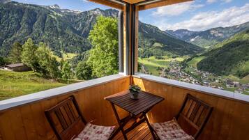 Ein Balkon mit Holzmöbeln, einem kleinen Tisch und Blick auf eine gebirgige Landschaft.