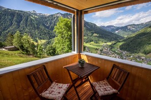 Un balcon agrémenté de meubles en bois, une petite table et une vue sur un paysage montagneux.