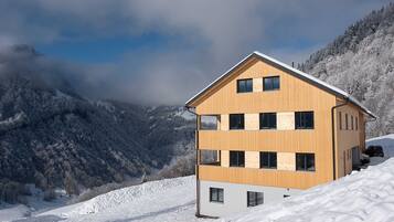 Ein mehrstöckiges Holzgebäude mit Balkonen vor einer verschneiten Berglandschaft.