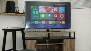 Litteänäyttöinen televisio on sijoitettu puiseen TV-telineeseen, ja sen alla on kaapelivastaan ja kaiutin.
