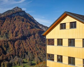 A multi-story building with a sloped roof, set against a mountainous backdrop.