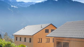 Deux bâtiments en bois, dotés de toits inclinés, entourés de verdure et avec des montagnes en arrière-plan.